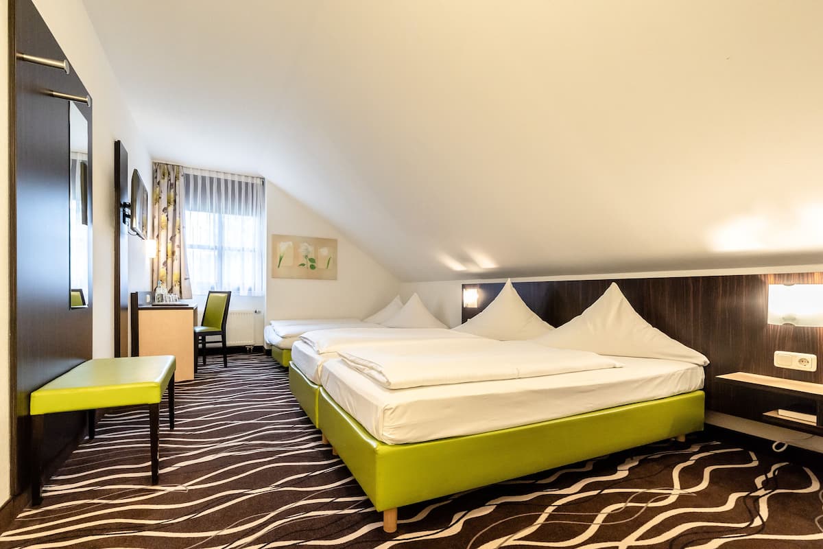 A hotel room with a green bed, a desk, a chair, and a window with curtains.