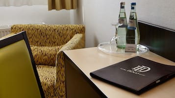 Una habitación de hotel con un sofá estampado con diseño de tigre, una mesa de madera con una bandeja de vidrio que contiene dos botellas de vino Gerolsteiner, y una carpeta negra con el logo de HD.