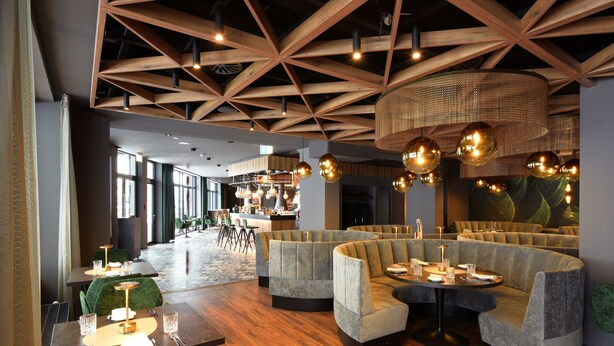 A modern hotel lobby with wooden ceiling beams, round tables, and green upholstered seating. - Hotel DEMAS Unterhaching (Unterhaching)