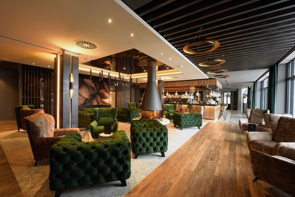Een moderne lobby met groene bekleden zitplaatsen, een centraal gelegen open haard en een bar.