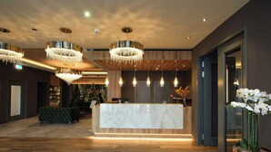 A modern reception area with a marble counter, wooden flooring, and multiple chandeliers. - Hotel DEMAS Unterhaching (Unterhaching)