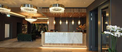 A modern reception area with a marble counter, wooden flooring, and multiple chandeliers.