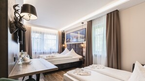 A hotel room with two beds, a dining table, a green chair, and a mounted deer head. - Hotel DEMAS Unterhaching (Unterhaching)