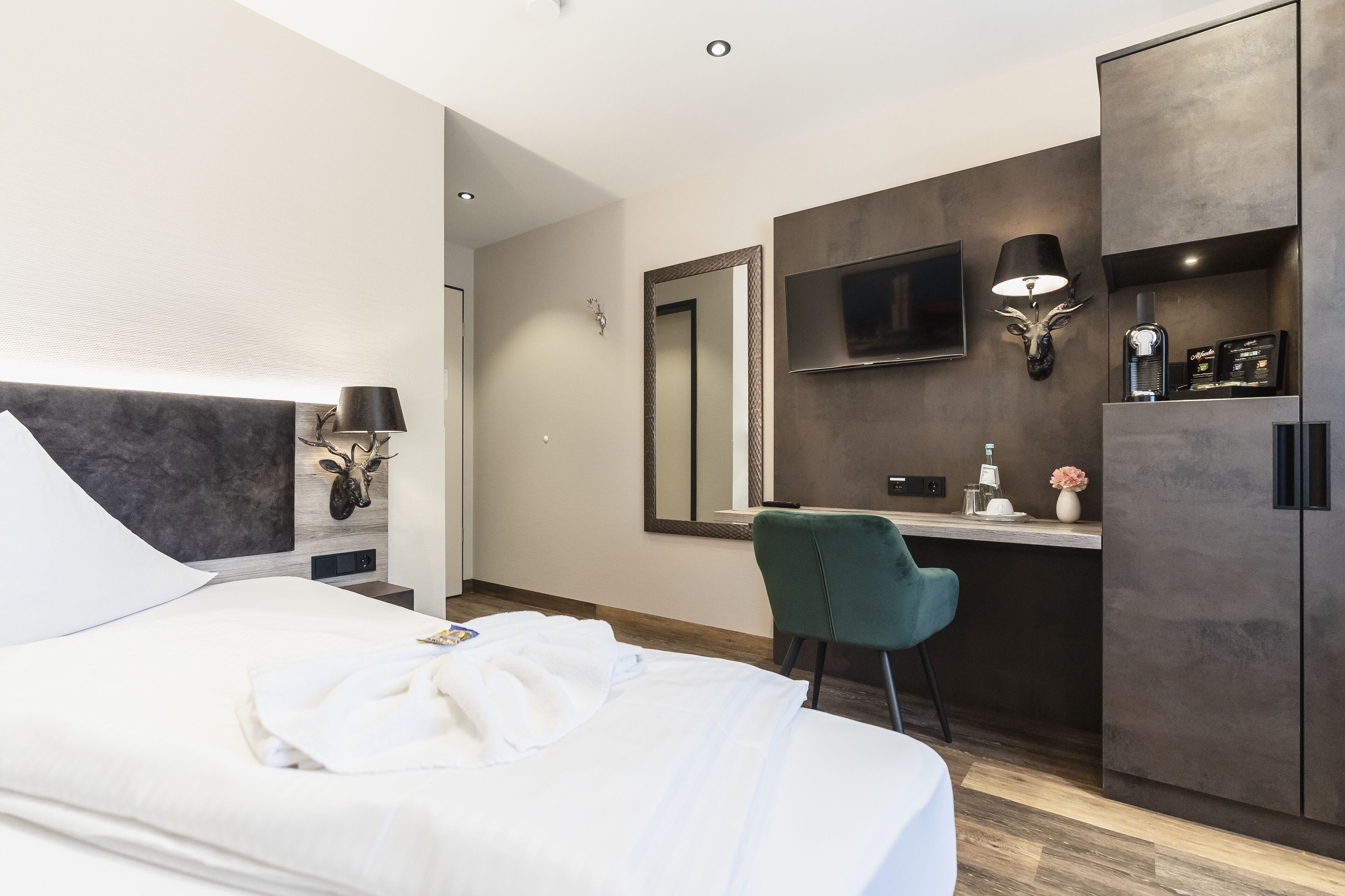 A modern hotel room with a large bed, a desk, a chair, a TV, and a minibar.