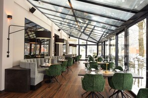 Een modern restaurant met een glazen plafond, groene bekleden stoelen en een houten vloer.