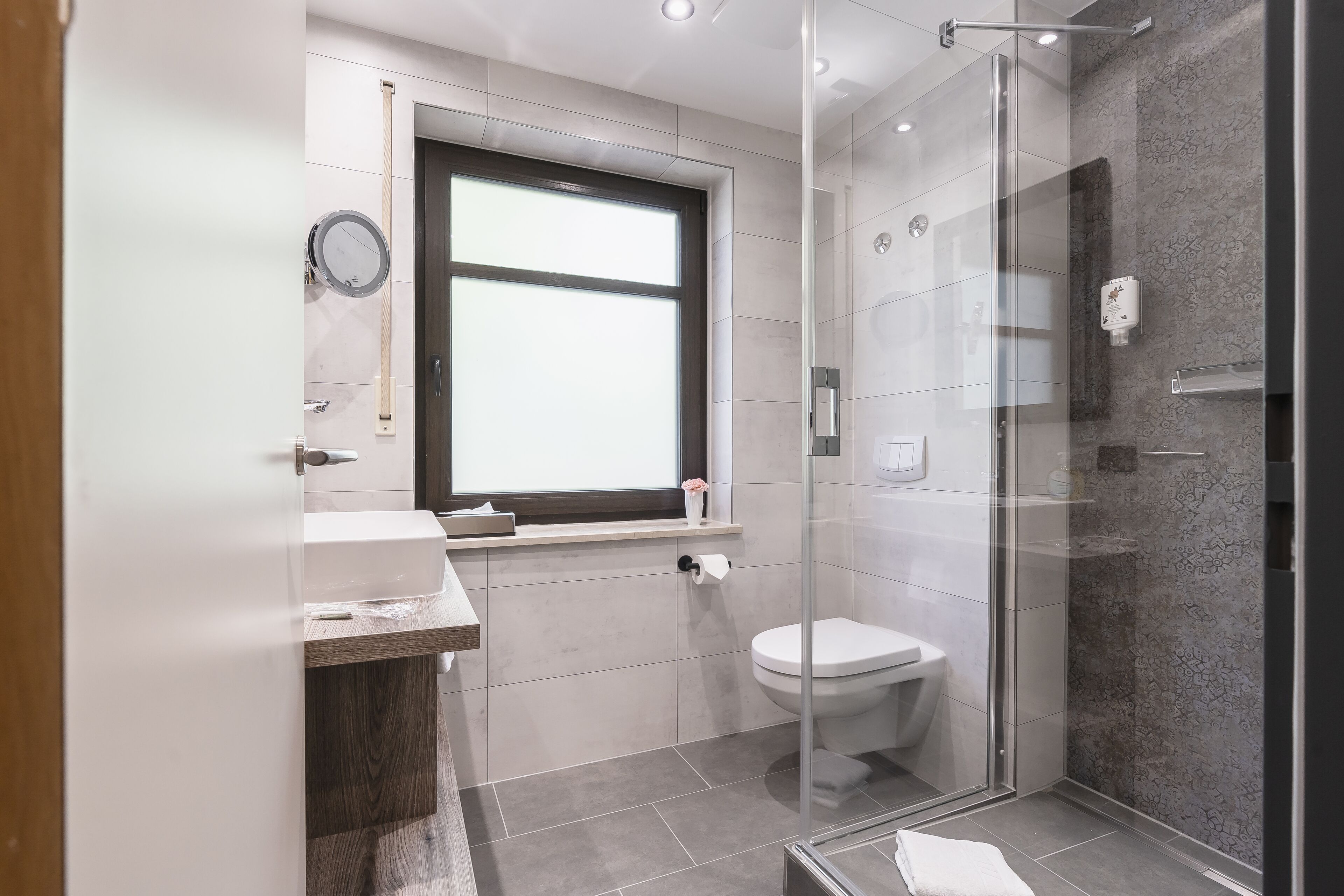 Un baño moderno con cabina de ducha de vidrio, inodoro y lavamanos con encimera de madera.