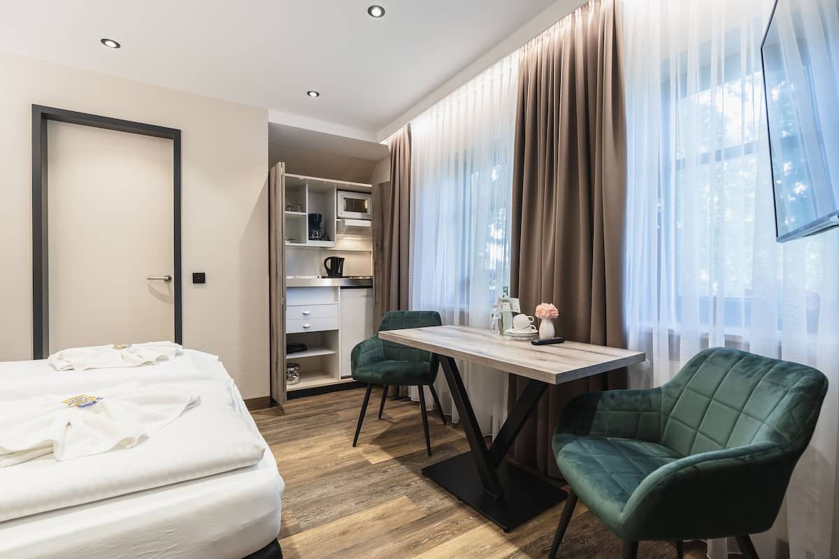 A hotel room with a bed, a desk, a chair, a wardrobe, and a window with curtains.