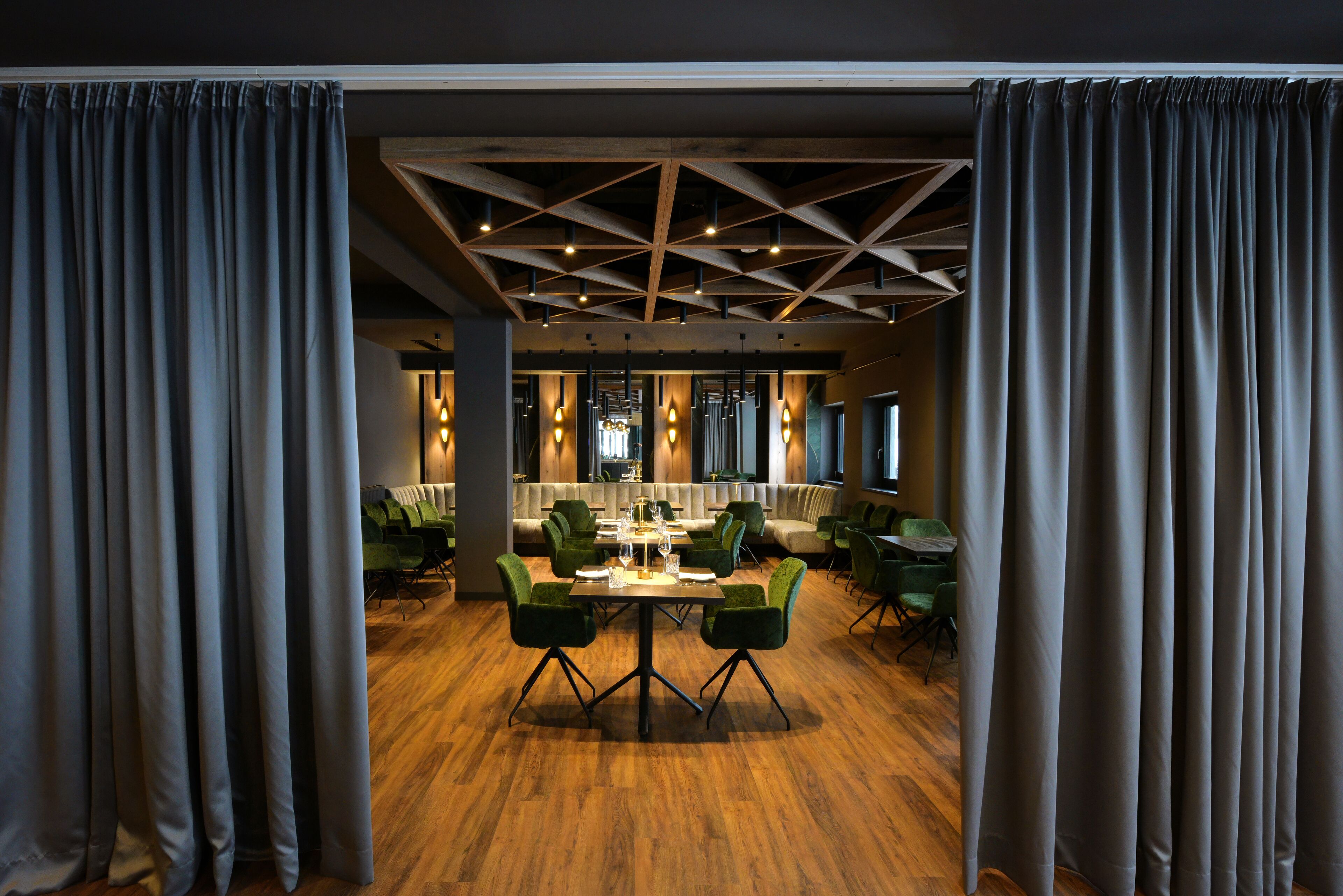 Un comedor moderno con suelo de madera, sillas tapizadas en verde y una mesa central dispuesta para comer.