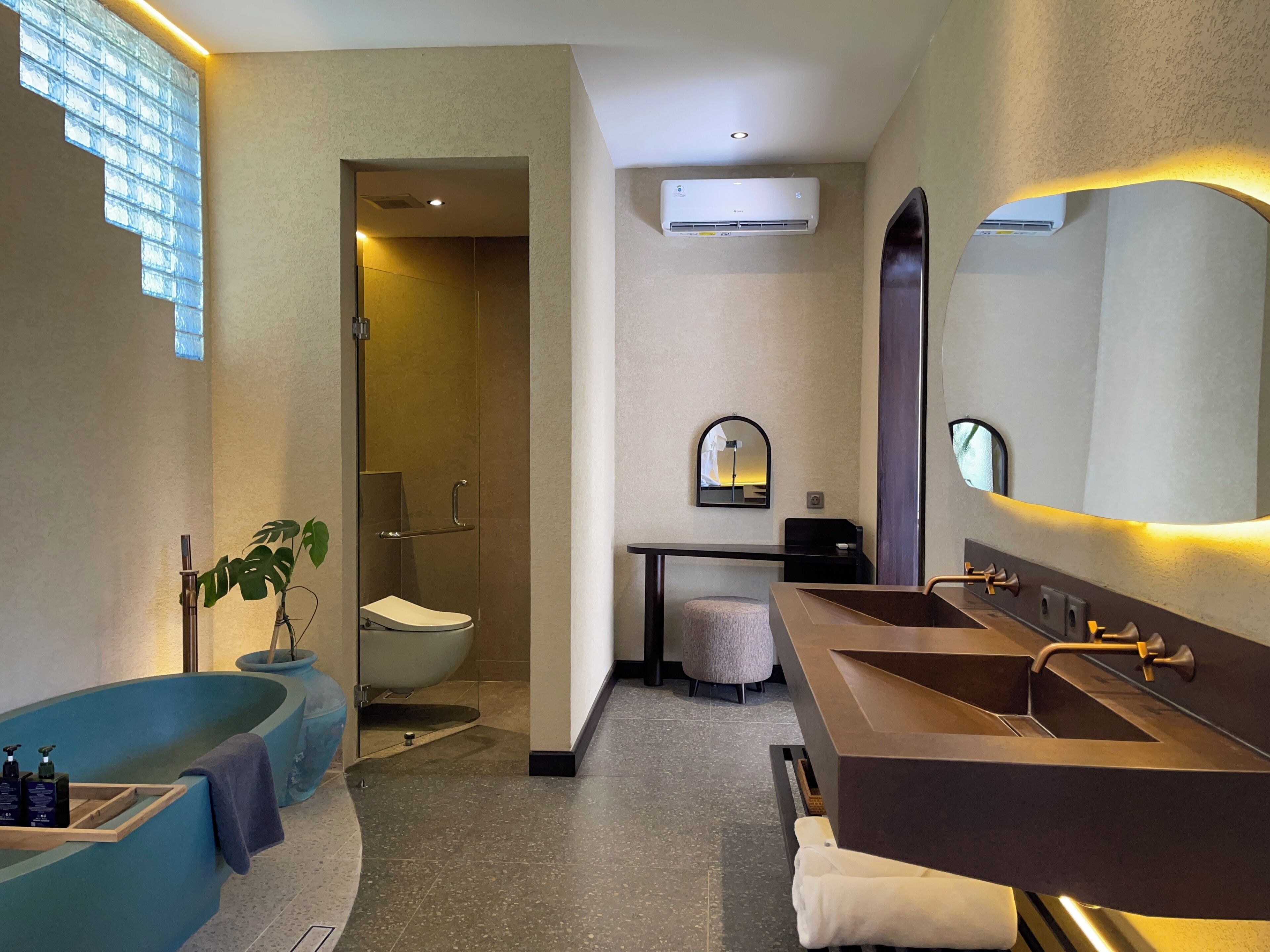 A modern bathroom with a bathtub, a large mirror, an air conditioning unit, and a shower.