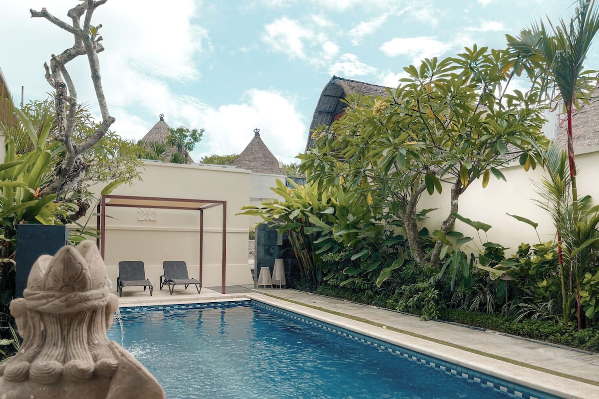 A swimming pool with lounge chairs, surrounded by tropical plants and a stone statue.