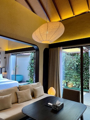 Une chambre d’hôtel moderne, dotée d’un canapé, d’une table et offrant une vue sur la verdure environnante.