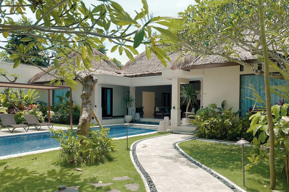 A pool area with lounge chairs, a pathway, and a thatched-roof structure.