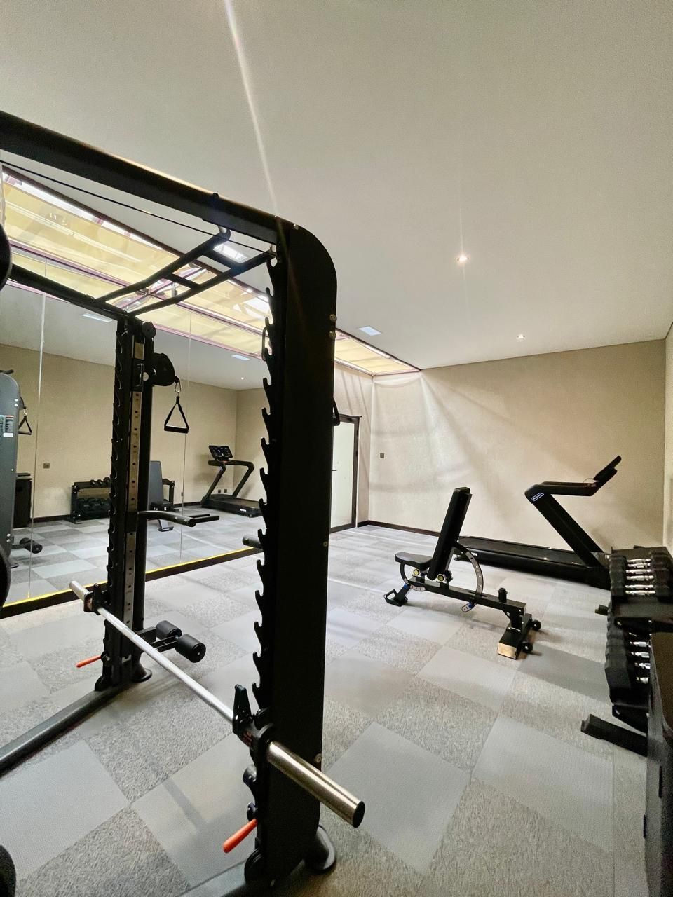 Un gimnàs amb equip de musculació, cintes de córrer i un mur mirall.
