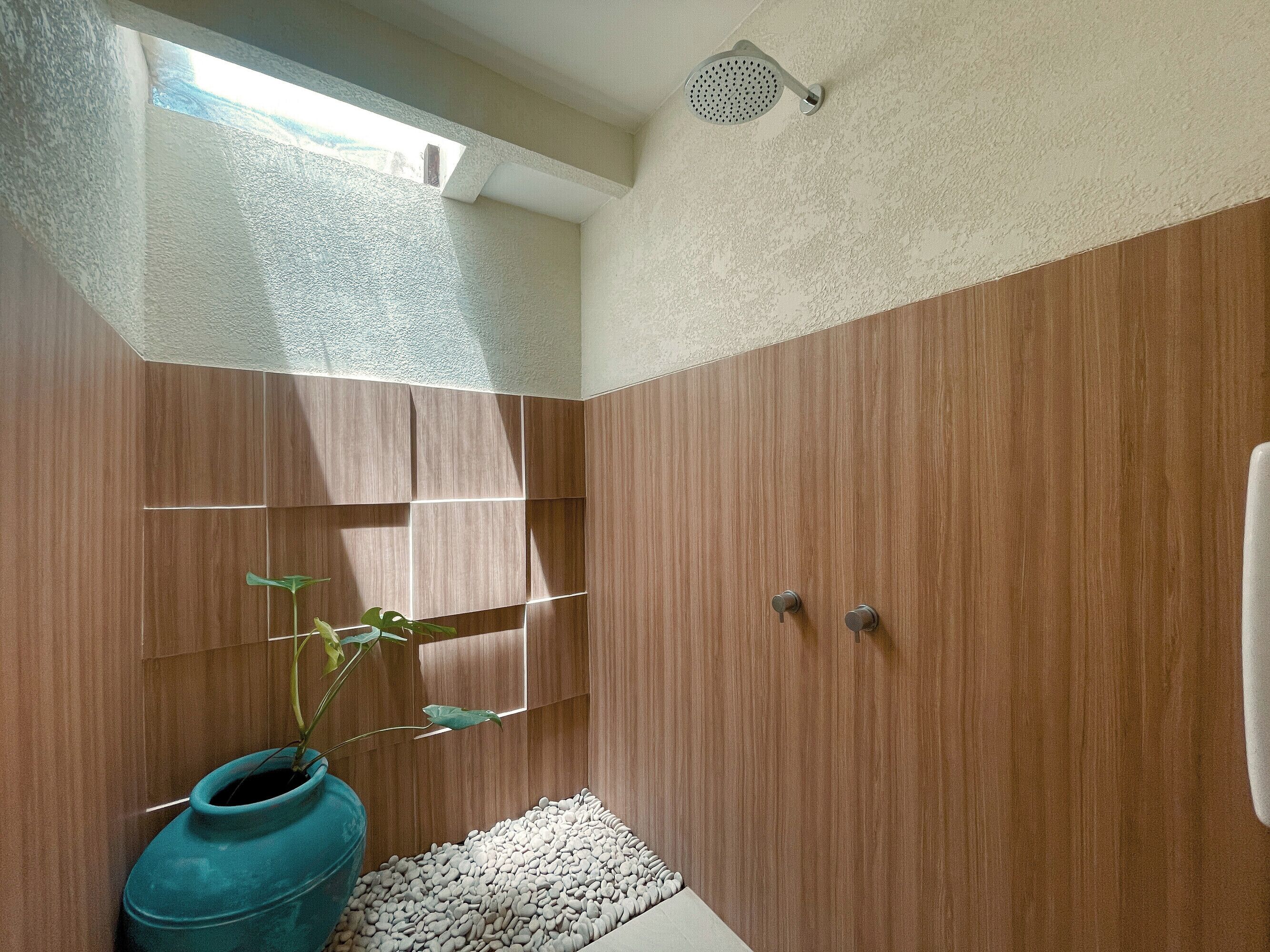 Un baño moderno con paneles de madera, un cabezal de ducha, una planta en maceta y un lecho de guijarros blancos.
