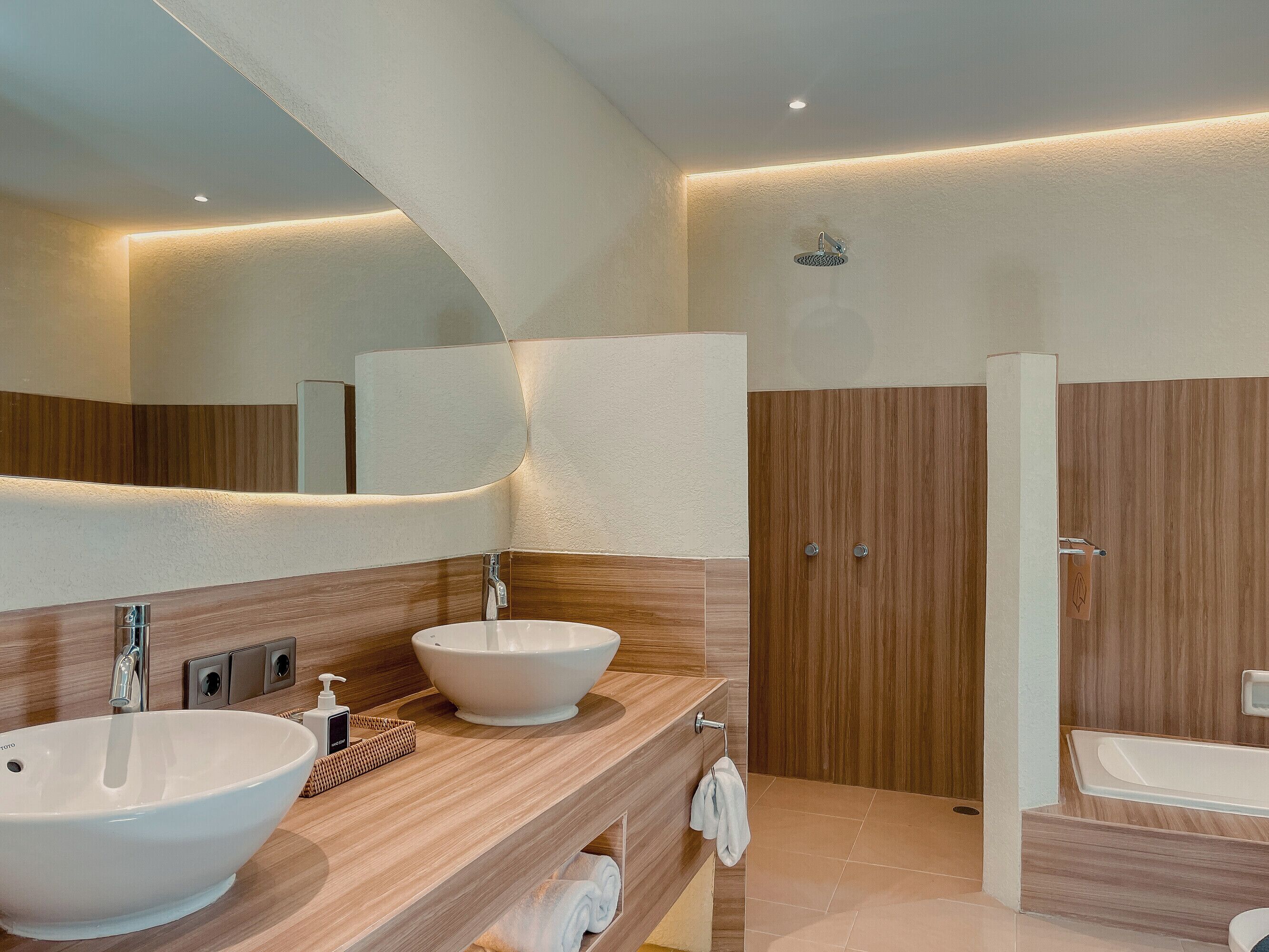 Une salle de bain moderne avec deux lavabos, un grand miroir, un lambris en bois et un espace douche.