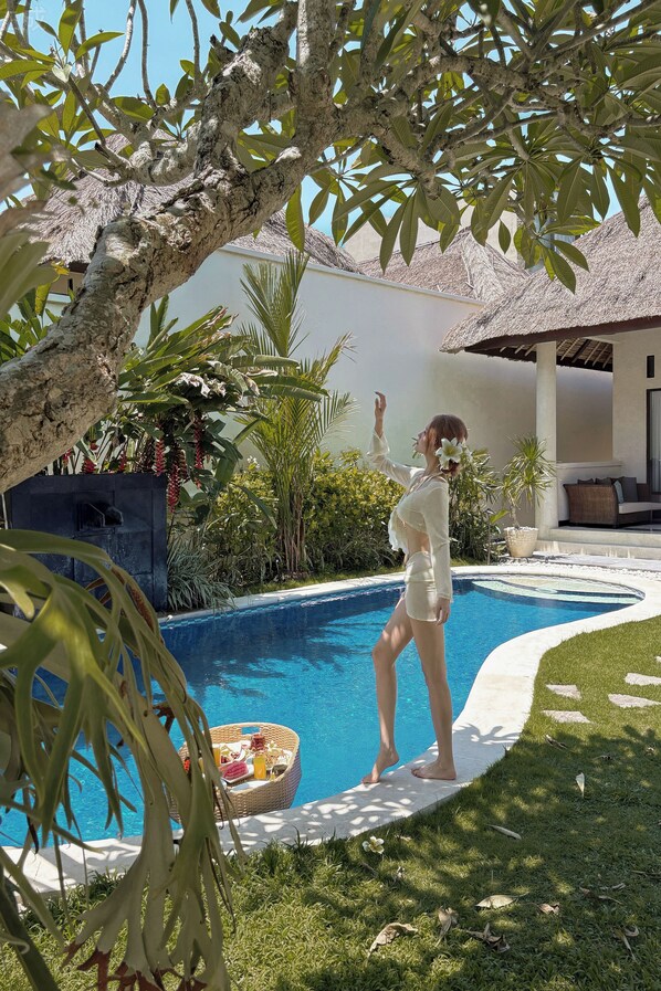 A poolside area with a thatched-roof structure, lush greenery, and a wicker basket with items. - Aruni Bali Jimbaran Boutique Villa (Jimbaran)
