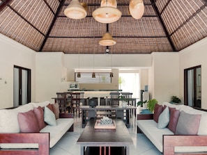 A spacious living area with a high ceiling, a dining table, and two sofas. - Aruni Bali Jimbaran Boutique Villa (Jimbaran)