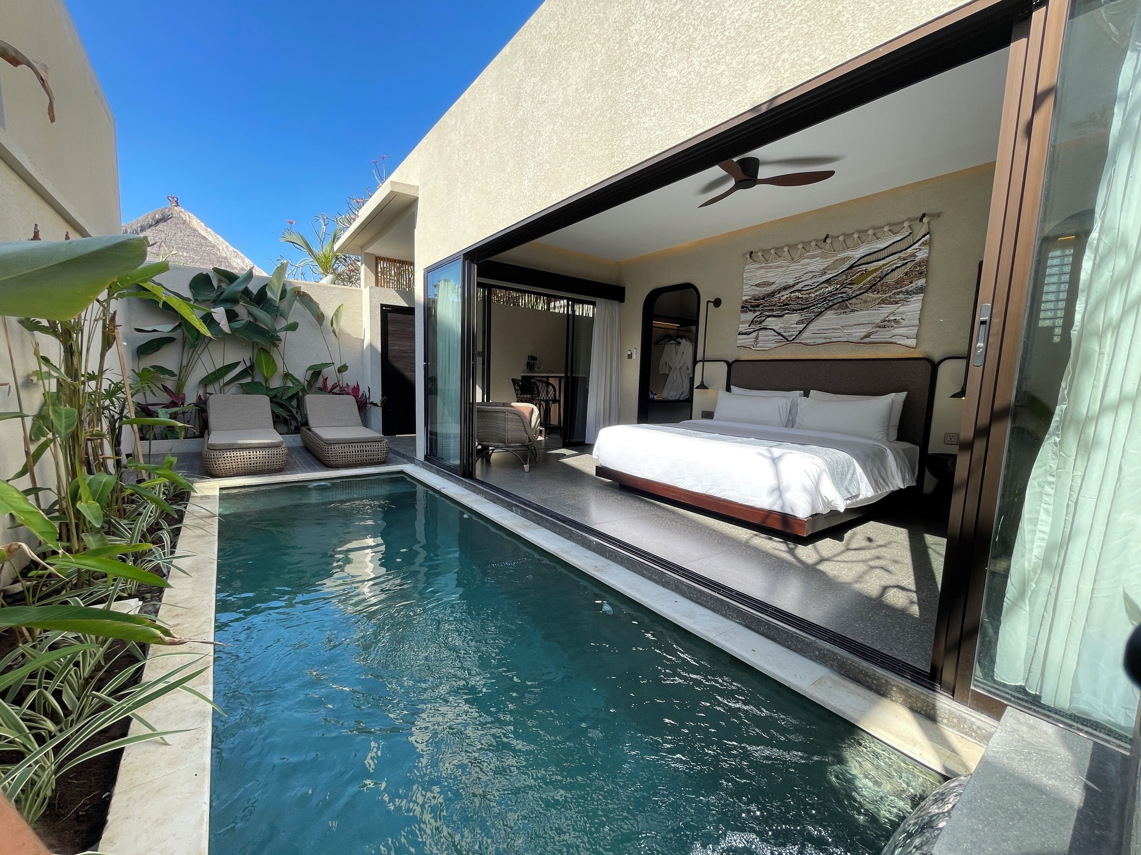 A modern hotel room with a large bed, a private balcony, and a swimming pool.