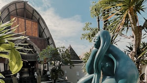 Eine Skulptur einer sitzenden Figur in einem Innenhof, im Hintergrund ein Gebäude.