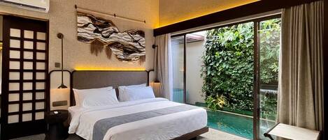 Un dormitorio con una cama grande, un ventilador de techo, una obra de arte en la pared y un ventanal corredero que da a un jardín.