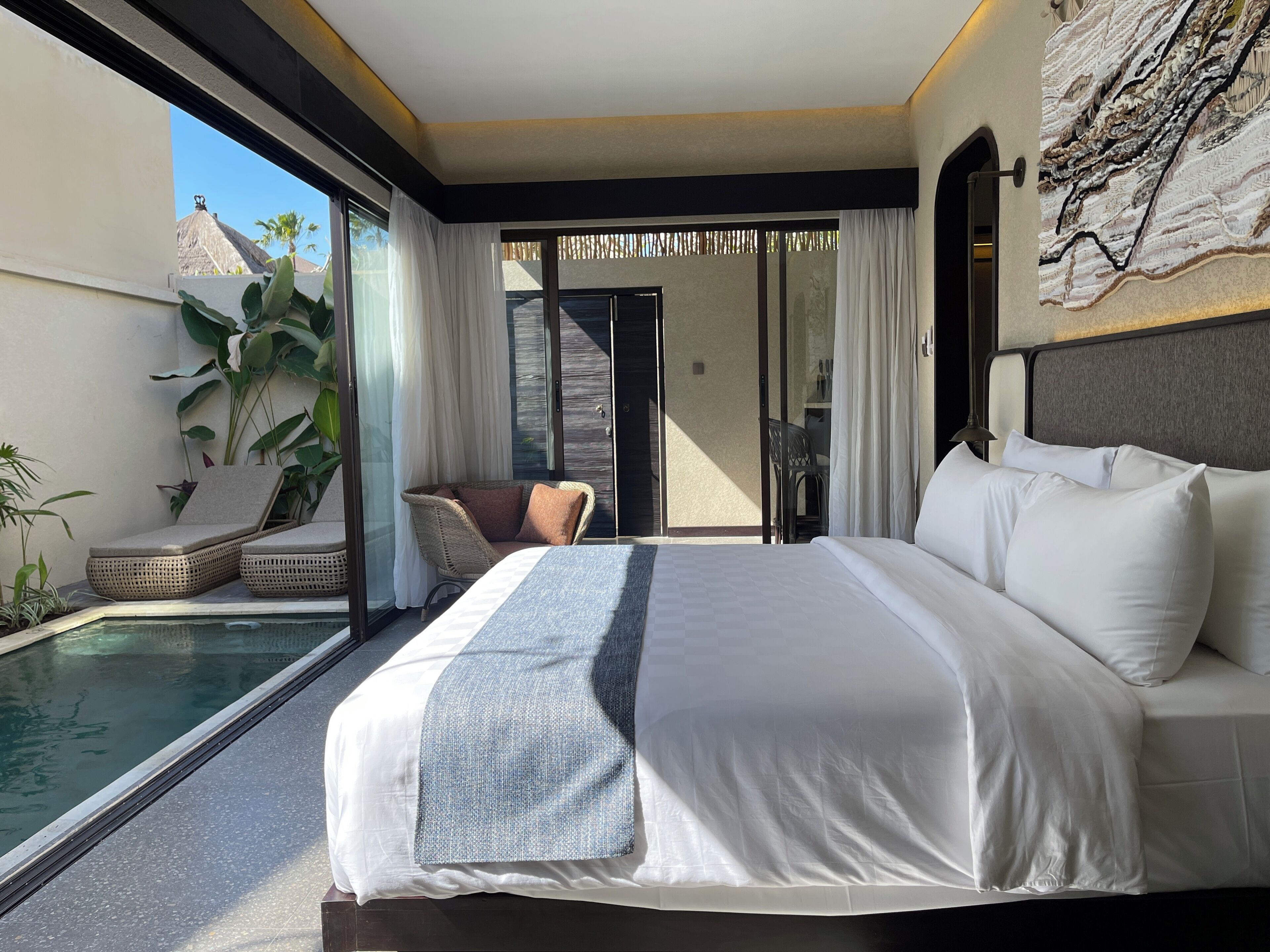 A modern hotel room with a large bed, a small balcony with a pool, and a view of the surrounding area.