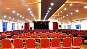 A conference room with rows of red chairs, a stage, and a high ceiling with recessed lighting. - Yuanda Business Hotel (Harbin)