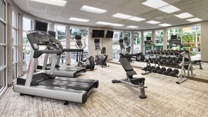 Un gimnasio con cintas de correr, elípticas y un estante de mancuernas.