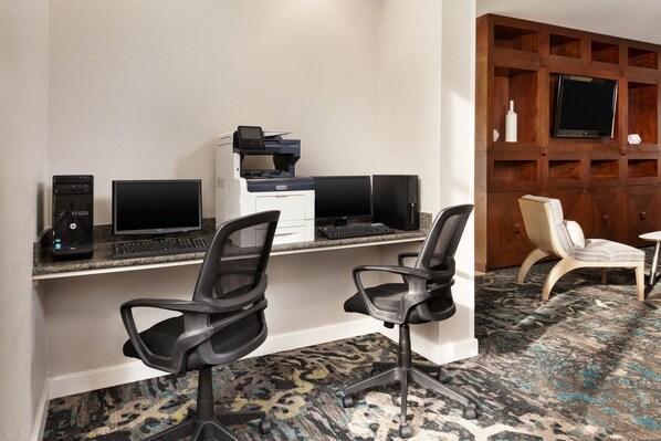 A hotel workspace with two desks, computers, printers, and office chairs.