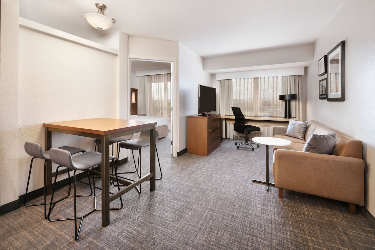 A hotel room with a dining area, a sofa, a TV, and a desk.