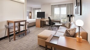Habitación de hotel con cama, escritorio con silla, sofá, una mesita y televisor.