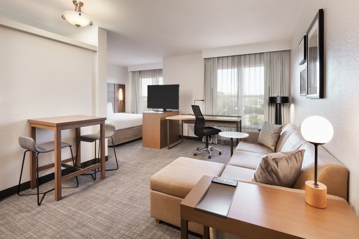 A hotel room with a bed, a desk with a chair, a sofa, a small table, and a TV.