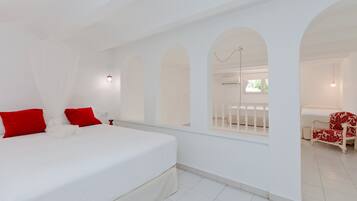 Un dormitorio con una cama grande, almohadones rojos, un dosel blanco y vistas a un balcón a través de una ventana arqueada.
