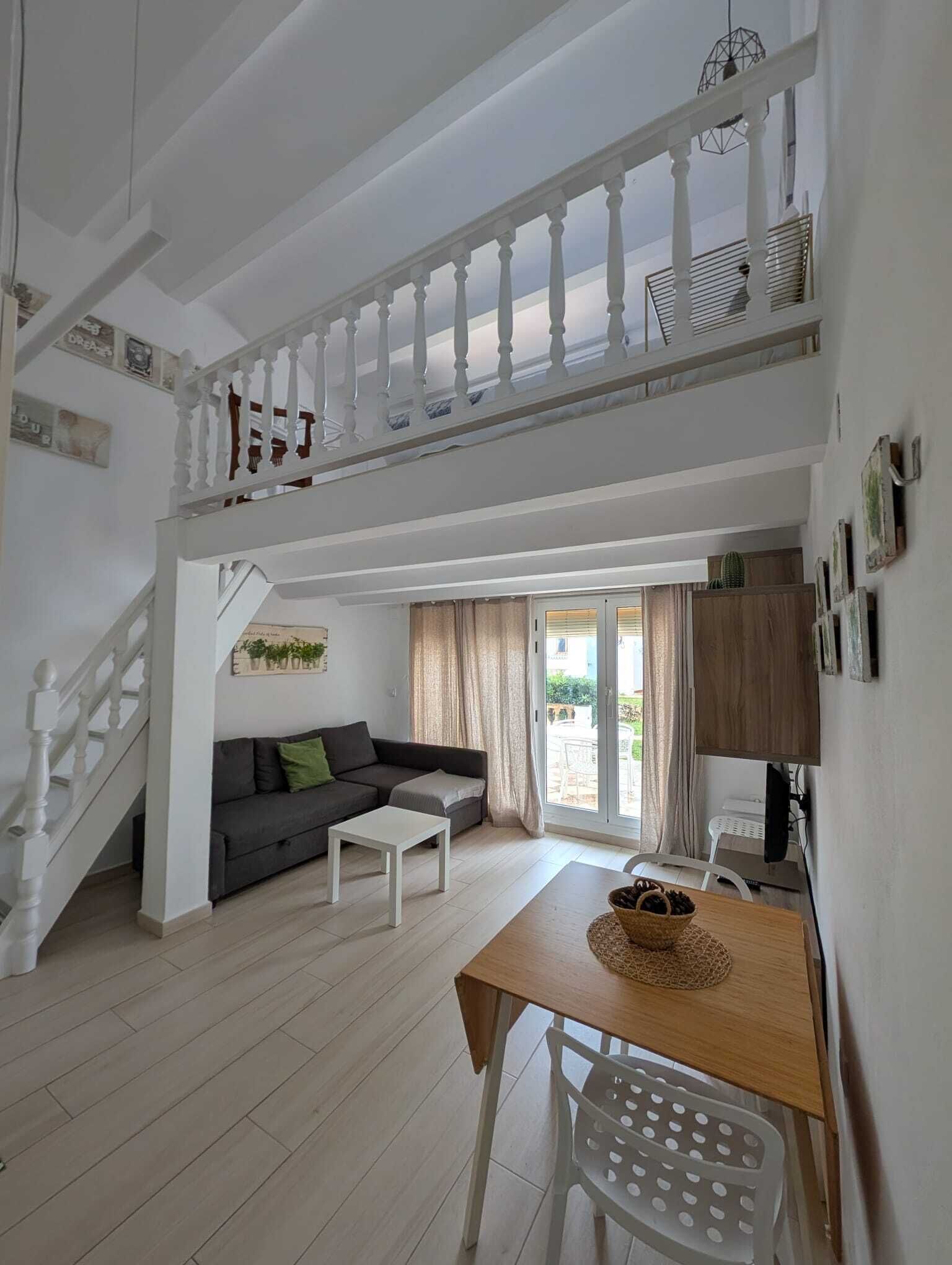 A spacious living area with a staircase leading to an upper level, a sofa, a coffee table, and a dining table with a basket of fruits.