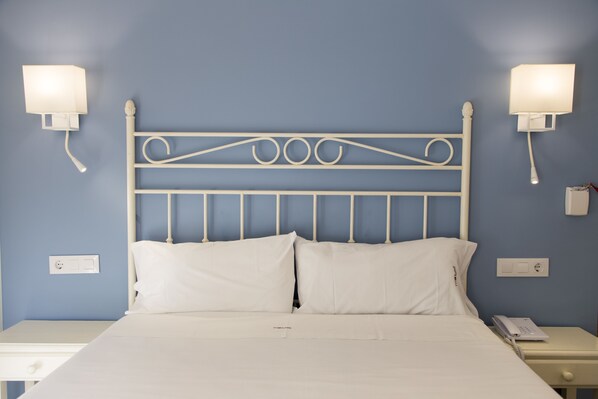 A neatly made bed with white linens, a white metal headboard, and bedside lamps on either side. - Hotelet de la Raconà (Denia)