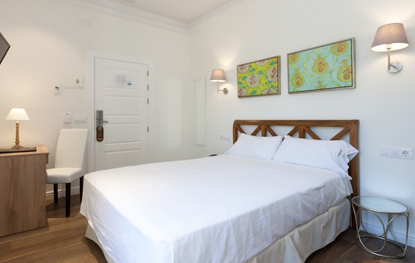 Un dormitorio ordenado con cama, mesita de noche, silla y lámparas de pared.