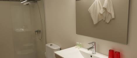 A bathroom with a shower, toilet, sink, and a mirror with towels.