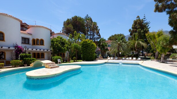 Una piscina con diseño geométrico en mosaicos, rodeada de sillas de descanso y palmeras.