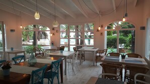 Un restaurante con mesas y sillas, ventanas amplias y lámparas colgantes.