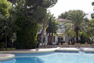 A pool with a decorative edge, surrounded by trees and a building with a tiled roof.
