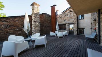 A wooden deck with white plastic chairs and umbrellas, stone walls, and a chimney.