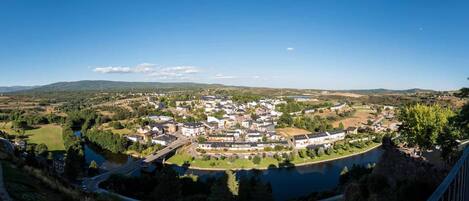 A panoramic view of a town with a river, surrounded by greenery and hills.