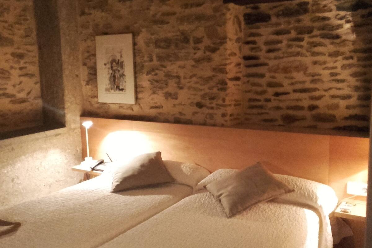 Habitación con paredes de piedra, una cama, una mesita de noche y una lámpara de pared.