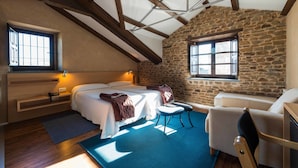 Un dormitorio con pared de piedra, vigas de madera, cama, una silla y un escritorio.