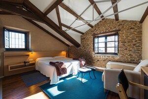 Un dormitorio con pared de piedra, vigas de madera, cama, una silla y un escritorio.
