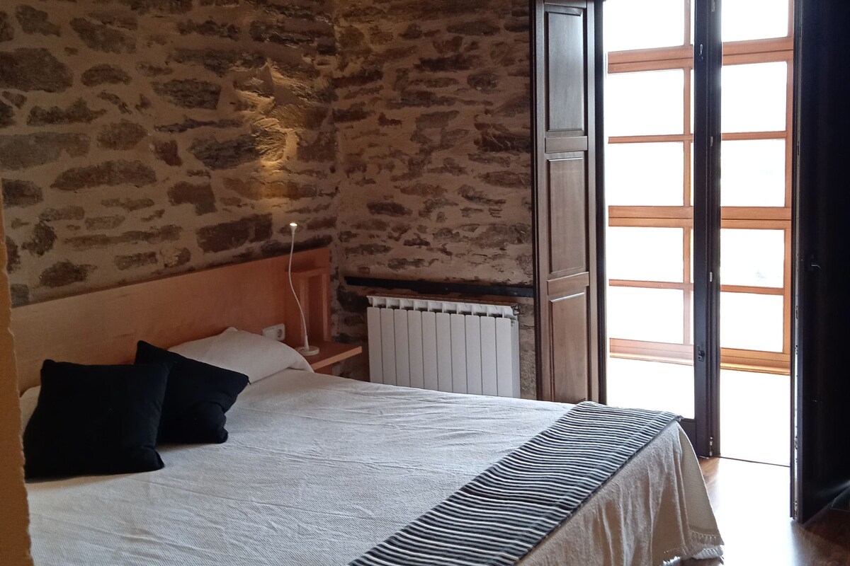 Een slaapkamer met een stenen muur, een bed met een gestreept dekbed, een radiator en een houten vloer.
