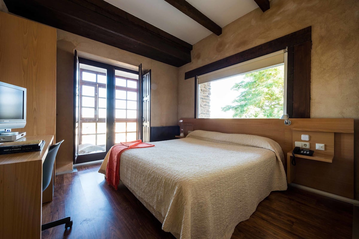 Un dormitorio con cama, un escritorio con computadora, una ventana y una puerta que da a un balcón.