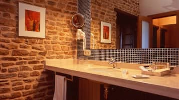 Une salle de bain avec un mur en pierre, un grand miroir, un lavabo et un tabouret.