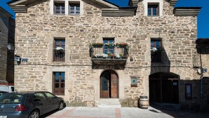 Un edificio de piedra con entrada central, ventanas y un balcón adornado con flores.