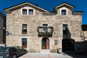 Un edificio de piedra con entrada central, ventanas y un balcón adornado con flores.