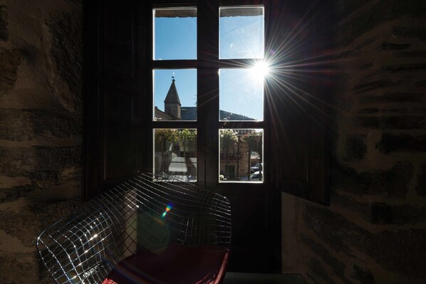 A room with a large window, a metal chair, and a stone wall.